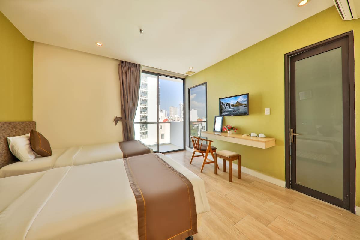 A hotel room with two beds, a desk, a chair, a TV, and a balcony with a city view.