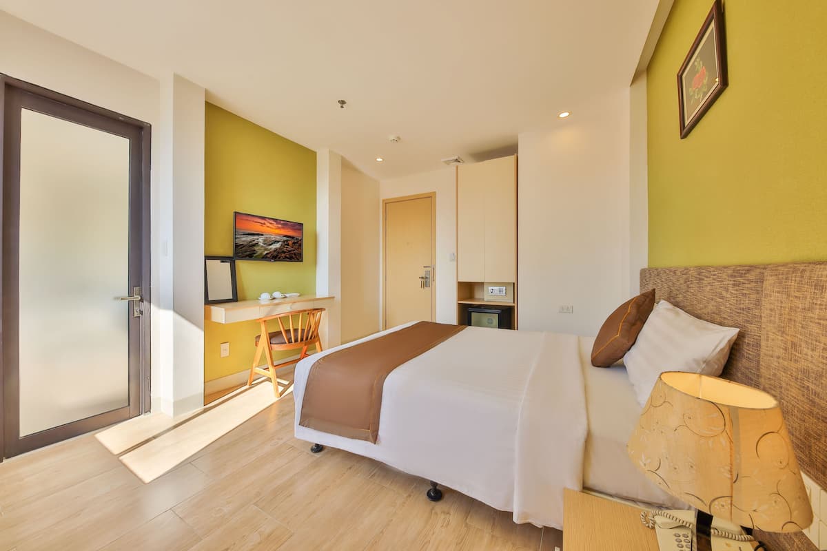 A hotel room with a bed, bedside lamp, and a desk with a chair.
