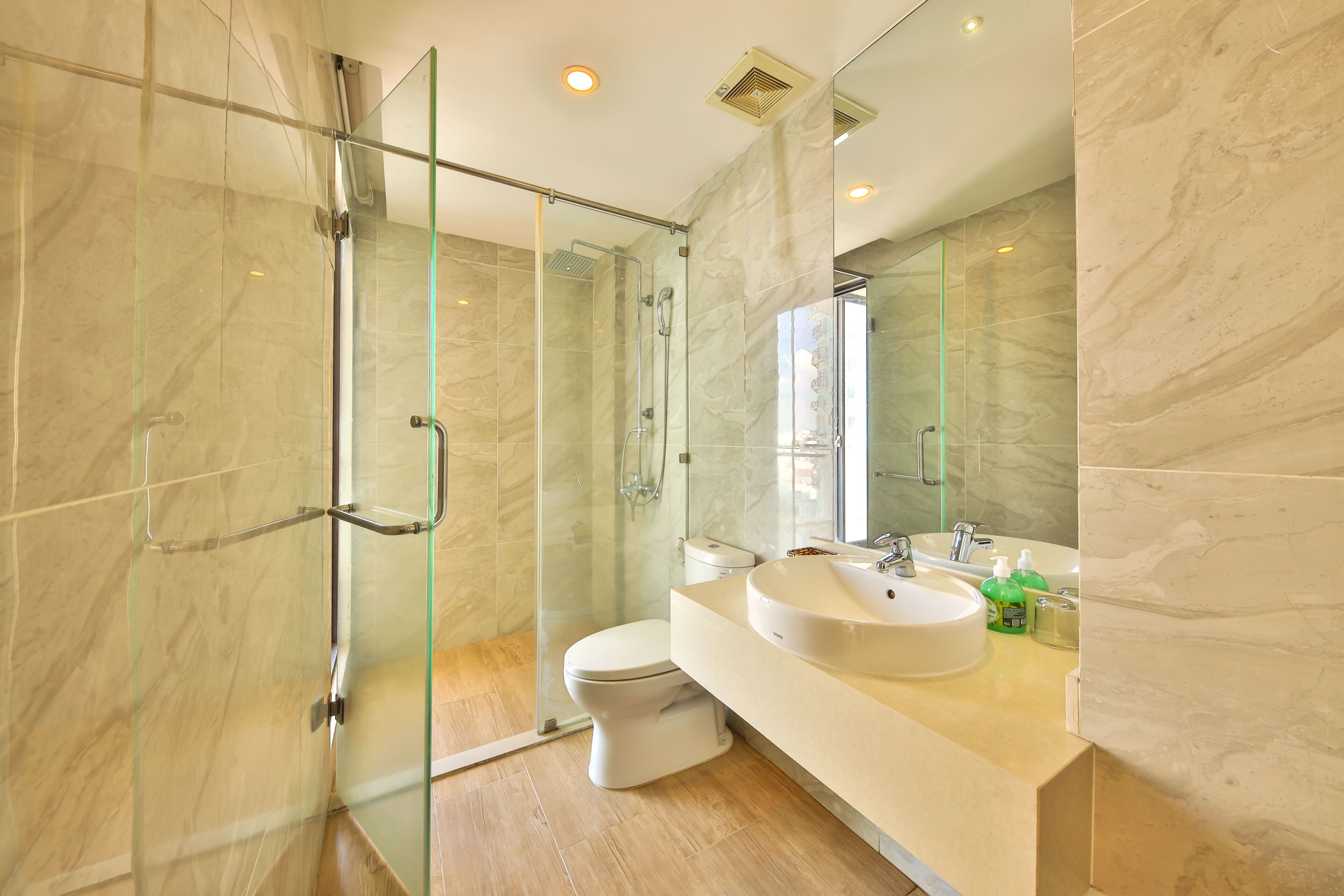 A modern bathroom with a glass-enclosed shower, a white toilet, and a marble-tiled vanity with a sink and mirror.