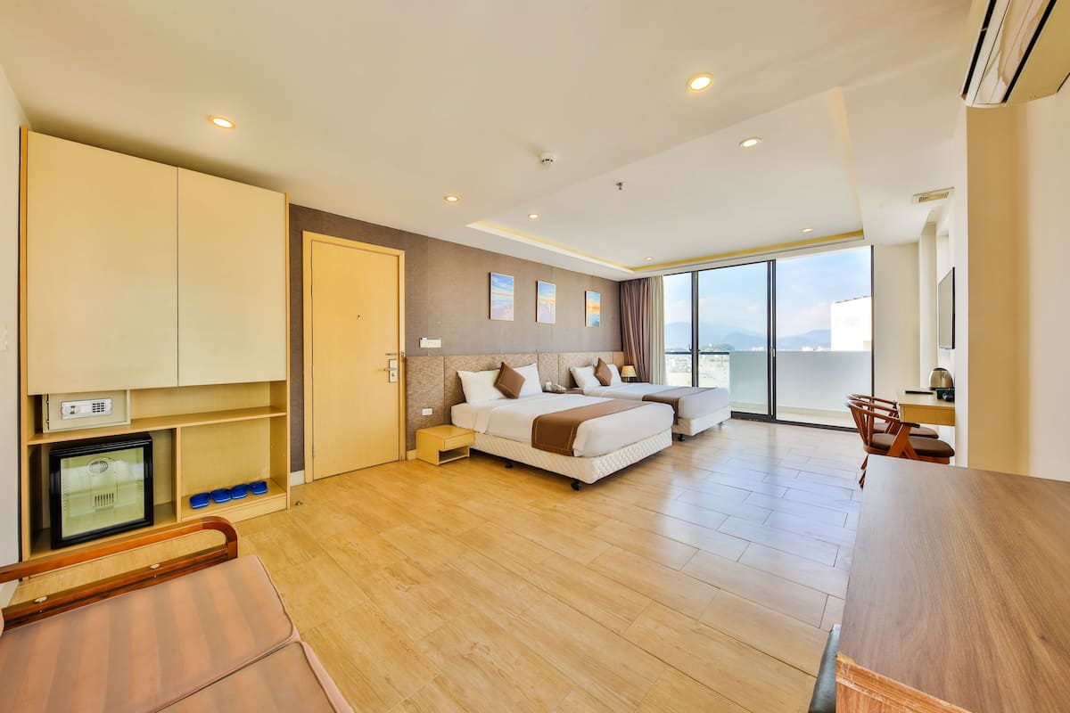 A modern hotel room with a large bed, a desk, and a balcony with a city view.