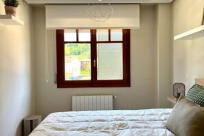 Une chambre à coucher avec un lit, un radiateur, une fenêtre avec des stores et un luminaire suspendu.