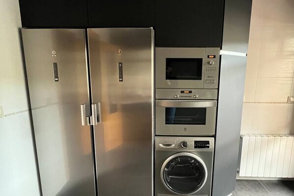 Une cuisine moderne équipée d’appareils électroménagers en acier inoxydable, notamment un réfrigérateur, un four, un four à micro-ondes et un lave-linge encastré.