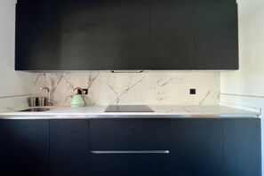 A kitchen with dark cabinets, a marble backsplash, and a modern kettle.