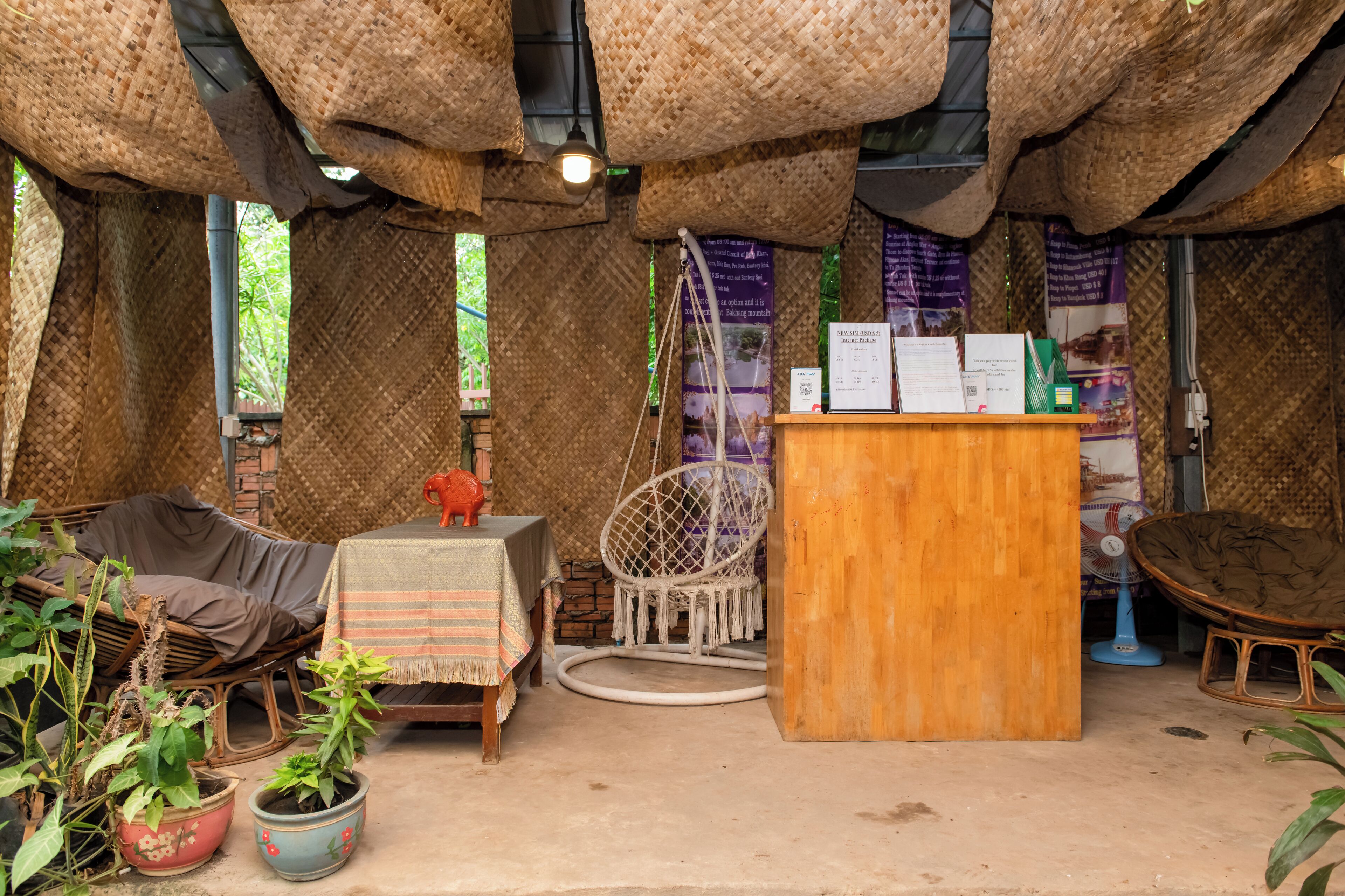 A rustic room with woven ceiling, wicker furniture, a wooden desk, and potted plants.