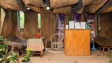 A rustic room with woven ceiling, wicker furniture, a wooden desk, and potted plants.