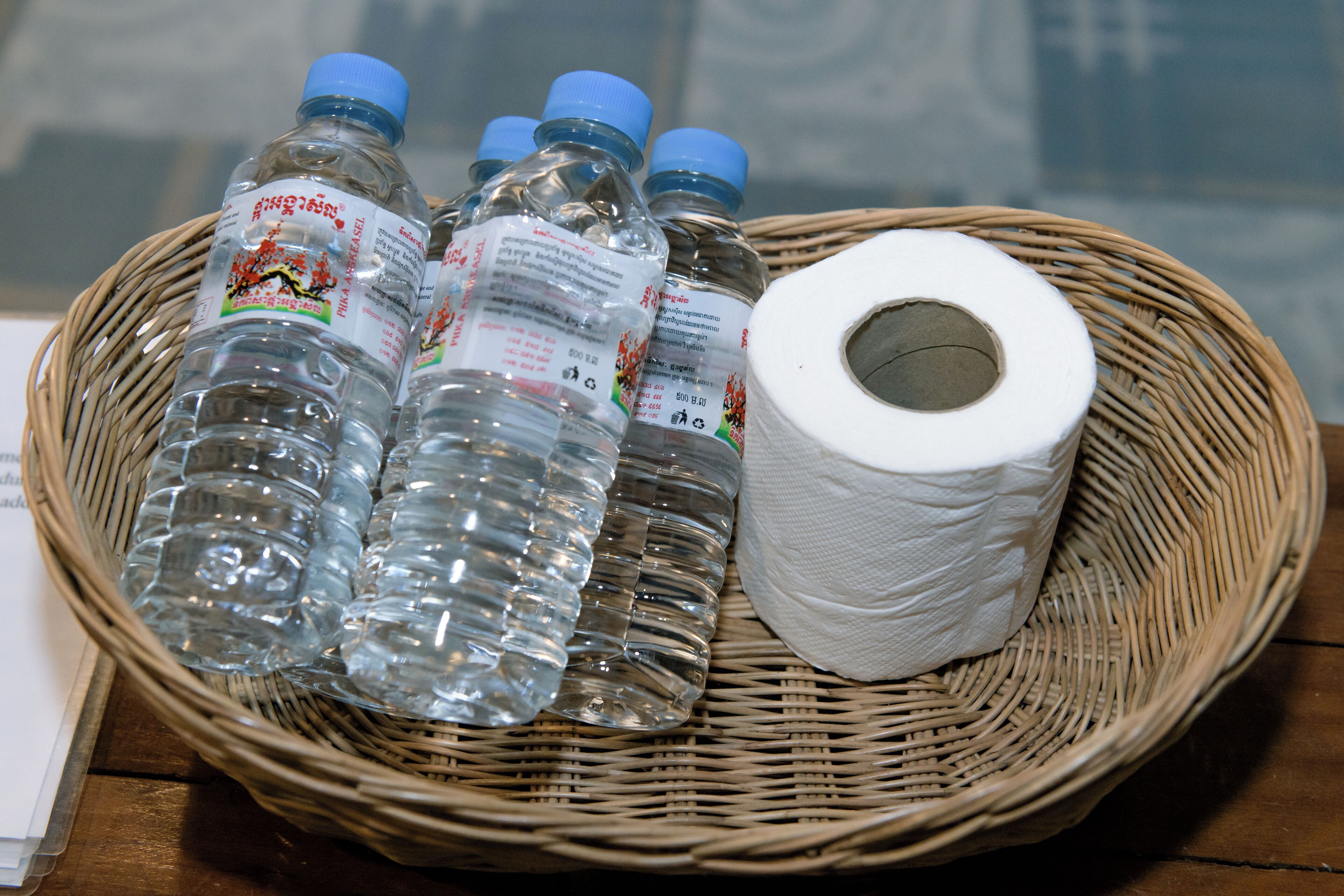 Un panier en osier contenant plusieurs bouteilles d’eau et un rouleau de papier toilette.