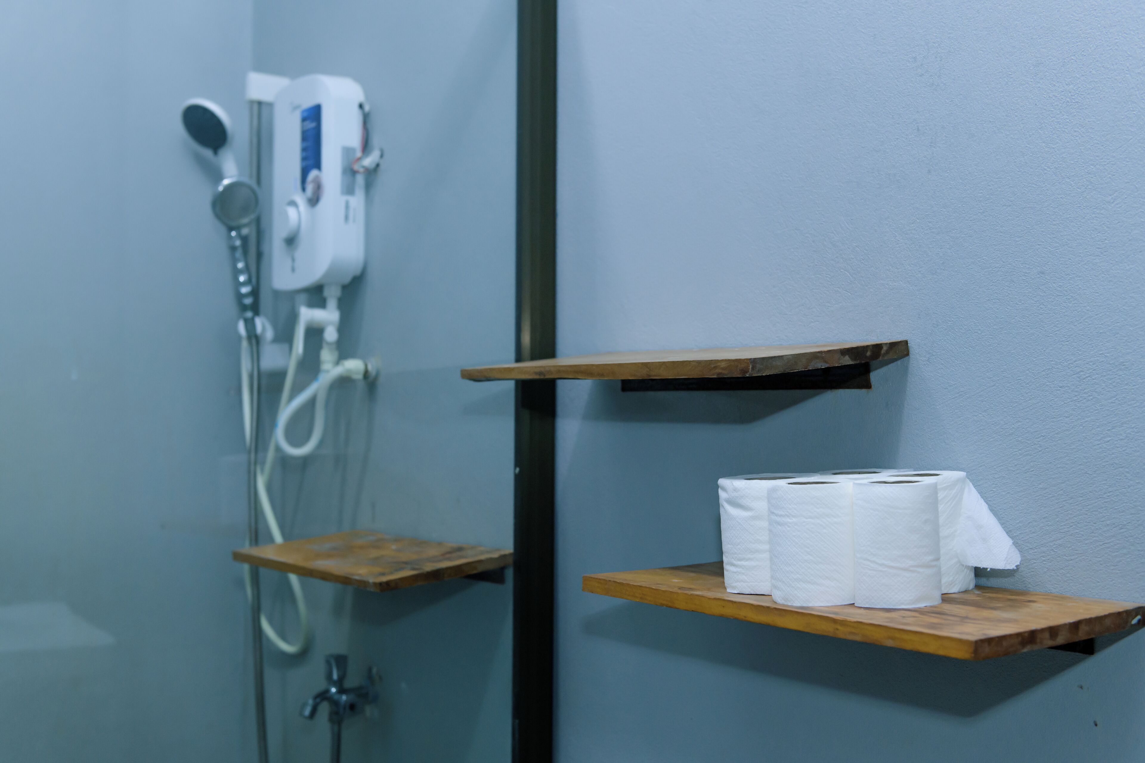 A bathroom with a shower, toilet paper on a shelf, and a towel rack.