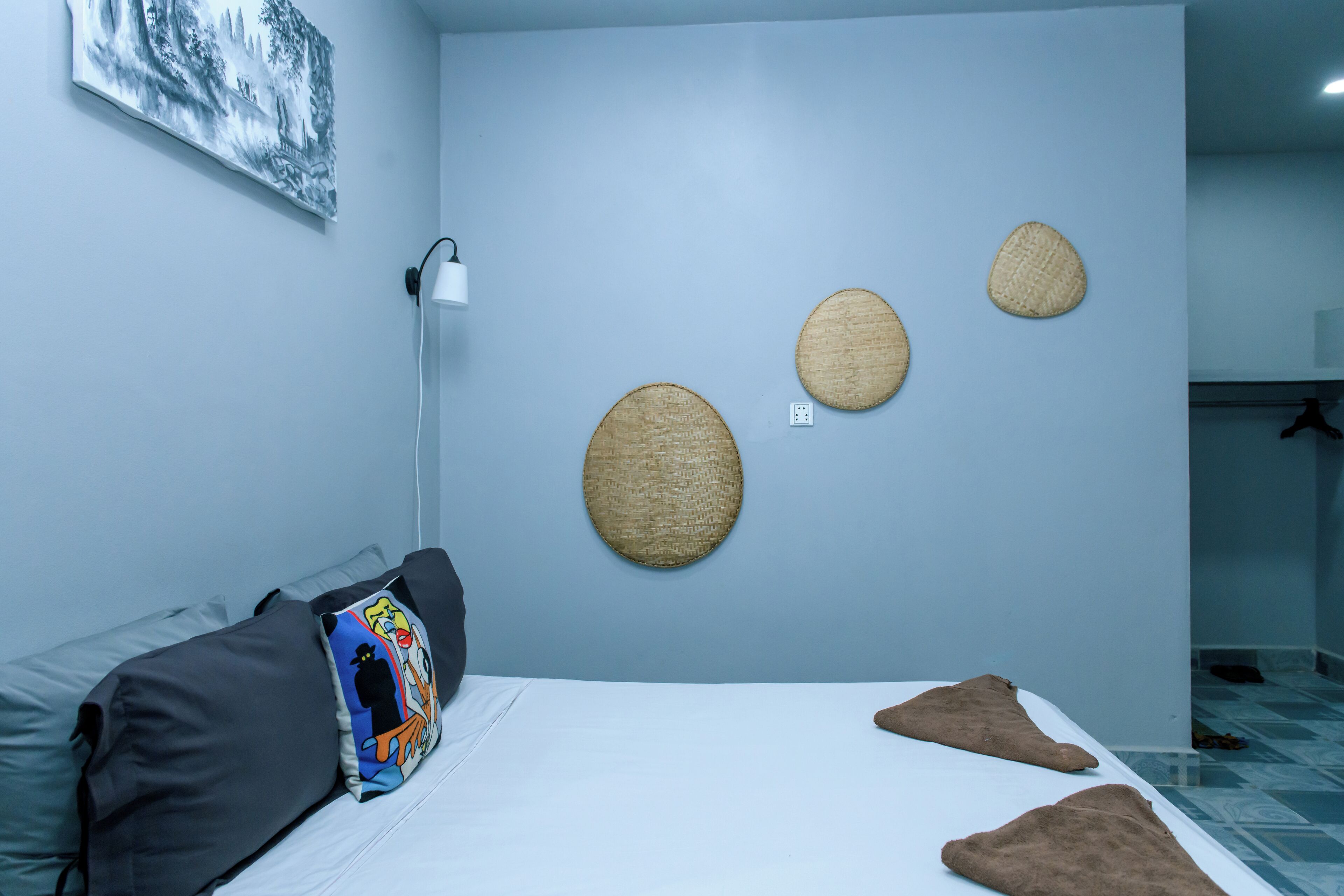 Een slaapkamer met een bed, een grijze bank, een muurlamp en drie geweven wanddecoraties.