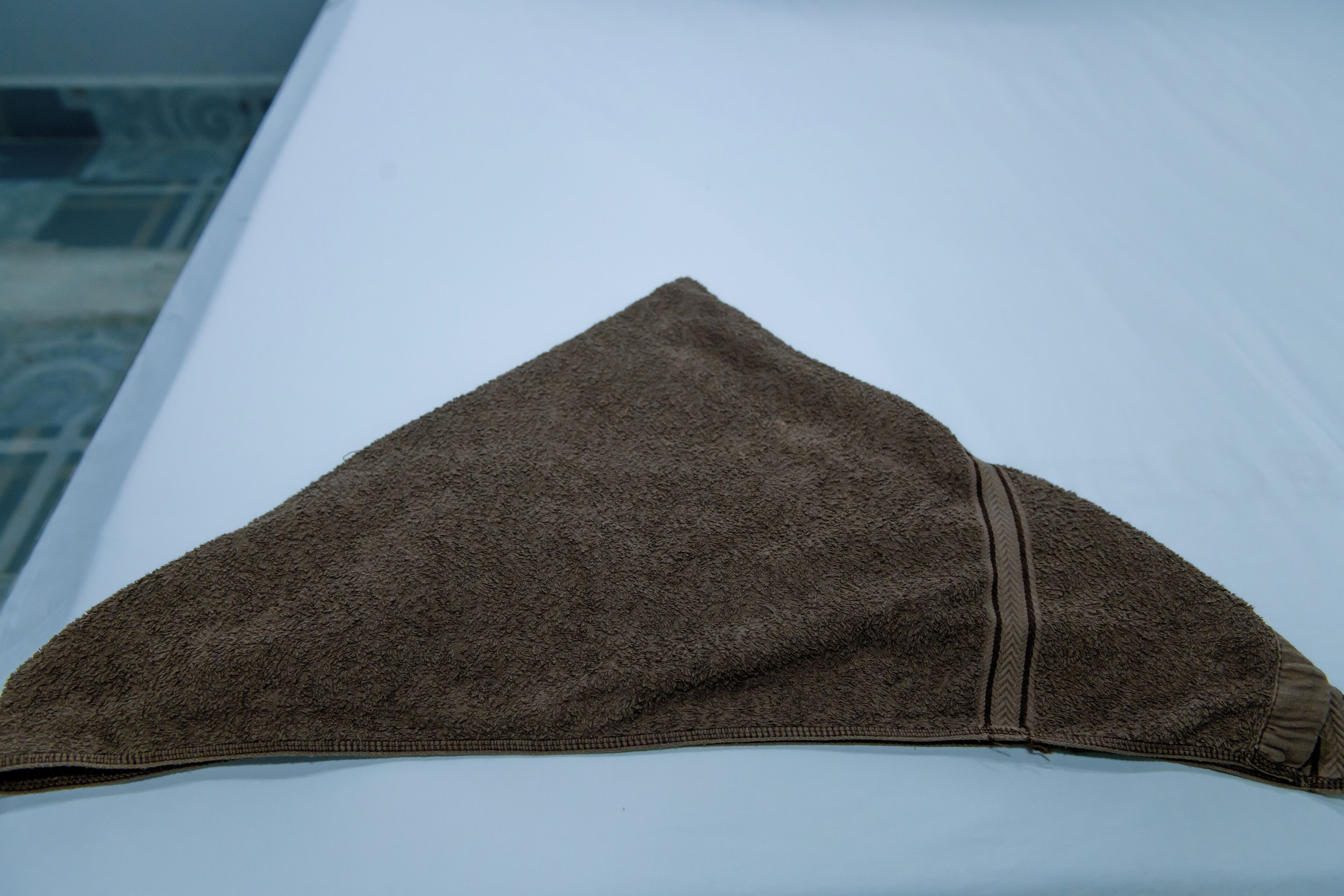 Un almohada triangular marrón sobre una cama blanca.