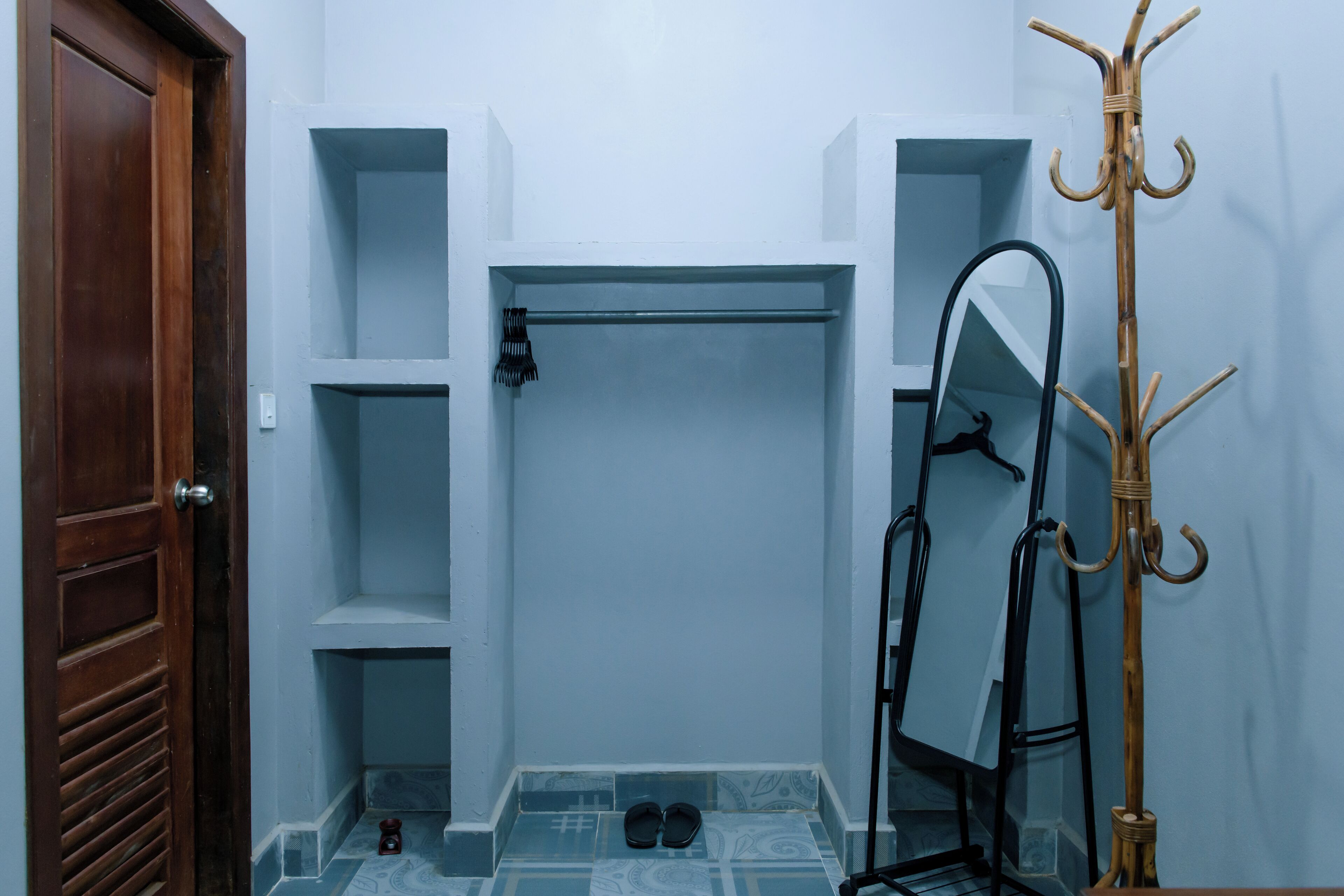 A bathroom with a wooden door, a mirror, a coat rack, and a pair of slippers on the floor.