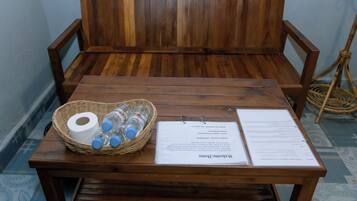 Un banco de madera con una cesta de agua embotellada y papel higiénico, y un menú sobre la mesa.