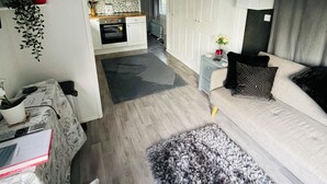 Un espace de vie compact comprenant un coin cuisine, un canapé agrémenté de coussins décoratifs et une petite table d’appoint avec un vase.
