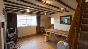 Ein Zimmer mit freiliegenden Holzbalken, einer hölzernen Bank, einem Fernseher und einem Fenster mit Vorhängen.