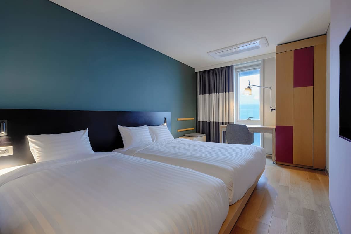 A hotel room with two beds, a desk, a chair, and a wardrobe.