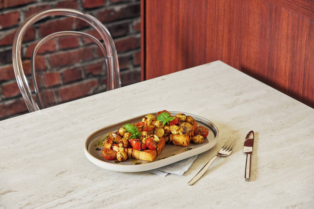 A plate of roasted vegetables on a marble table with a fork and knife beside it.