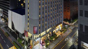 Ett högt hotell med en framträdande skylt med texten ”SONO MOON” högst upp, med en modern arkitektonisk design som kännetecknas av vertikala linjer och upplysta fönster.