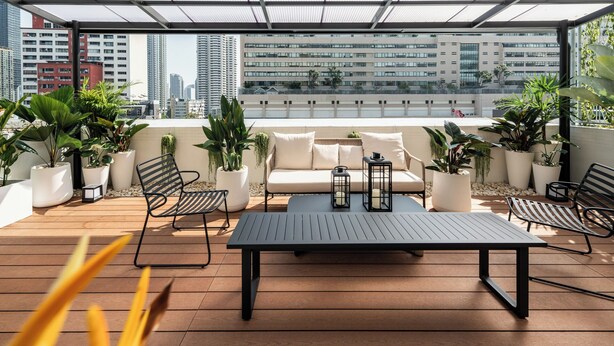 Eine Dachterrasse mit Glasüberdachung, Sitzgelegenheiten im Freien und Topfpflanzen.