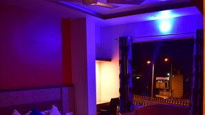 A hotel room with a large bed, a ceiling fan, and a view of the outside at night. - HOTEL JYOTI PALACE (Biaora)