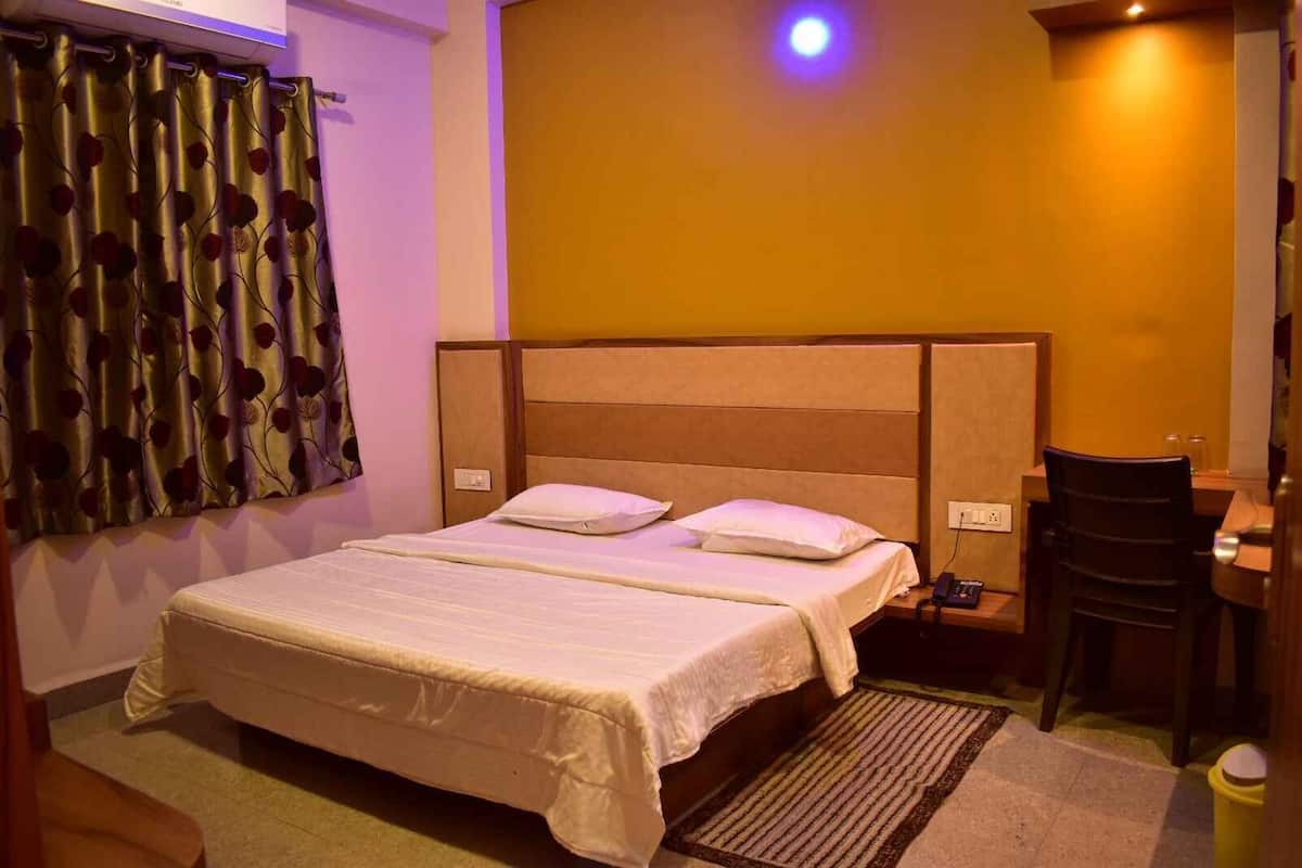 A hotel room with a large bed, a bedside table with a lamp, a chair, and a small desk with a telephone.