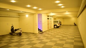 A parking garage with a checkered floor, a scooter, and a vehicle in the background. - HOTEL JYOTI PALACE (Biaora)