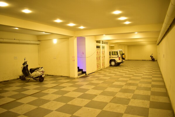 A parking garage with a checkered floor, a scooter, and a vehicle in the background. - HOTEL JYOTI PALACE (Biaora)