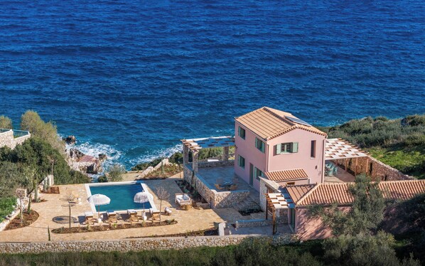 A coastal villa with a swimming pool, stone patio, and a view of the sea.