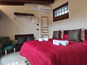 A hotel room with a large bed, a green armchair, a wooden headboard, and a window with a view.