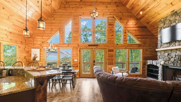 A log cabin interior with a kitchen, dining area, and a stone fireplace. - Spectacular Log Cabin Mtn Views Hot Tub Pool Table Theater Room Spa/Sauna (McGaheysville)