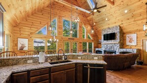A spacious kitchen with granite countertops, wooden cabinets, and a stone fireplace. - Spectacular Log Cabin Mtn Views Hot Tub Pool Table Theater Room Spa/Sauna (McGaheysville)