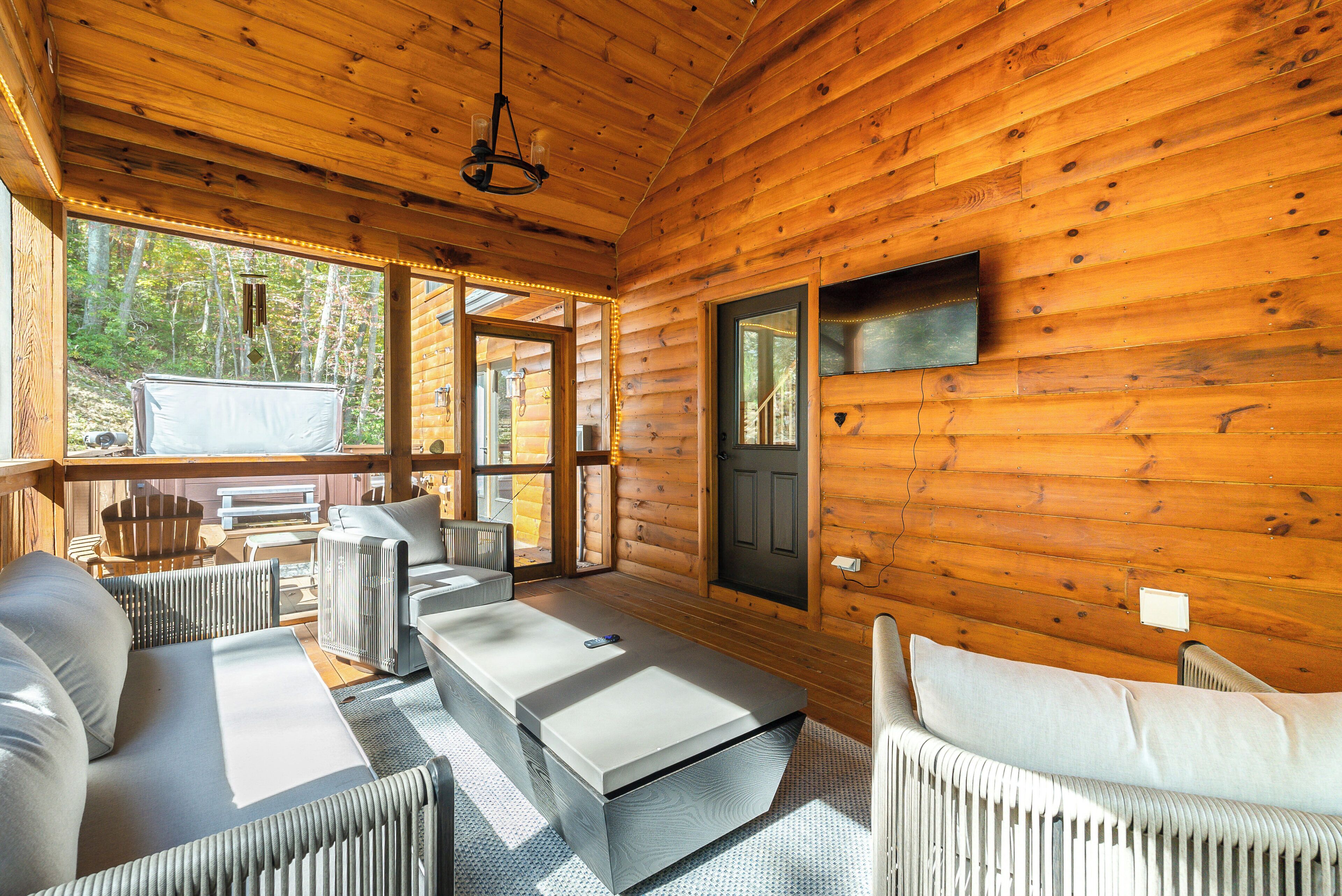A log cabin interior with a sofa, a coffee table, and a view of the forest through large windows.