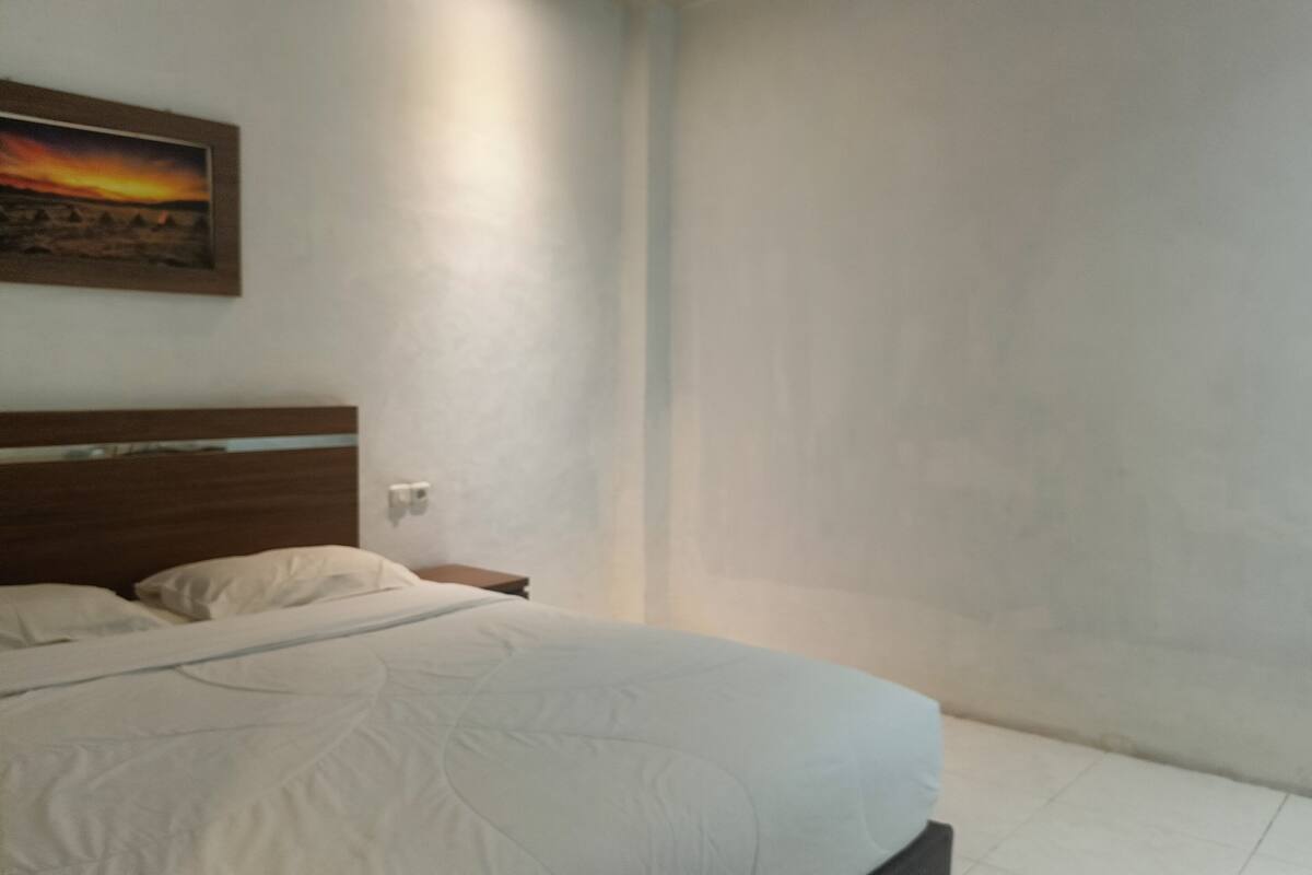 Une chambre à coucher avec un lit, une table de chevet, un tableau accroché au mur et un mur uni.