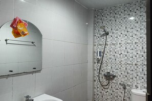A bathroom with a white sink, a mirror, a shower with a tiled wall, and a toilet. - Hotel O Erbee Inn (Makassar)