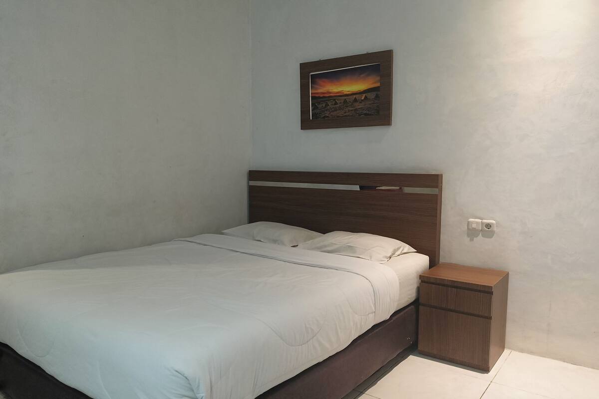Une chambre avec un lit simple, une table de chevet et un tableau encadré au mur.