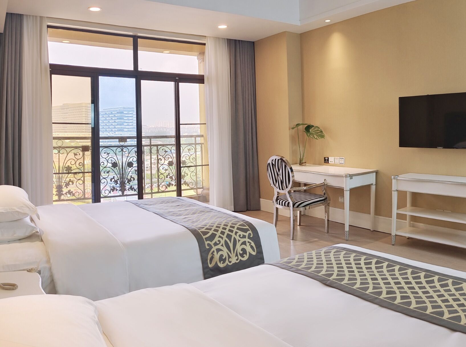 Habitación de hotel con dos camas, un escritorio, una silla, un televisor y un balcón con vistas.