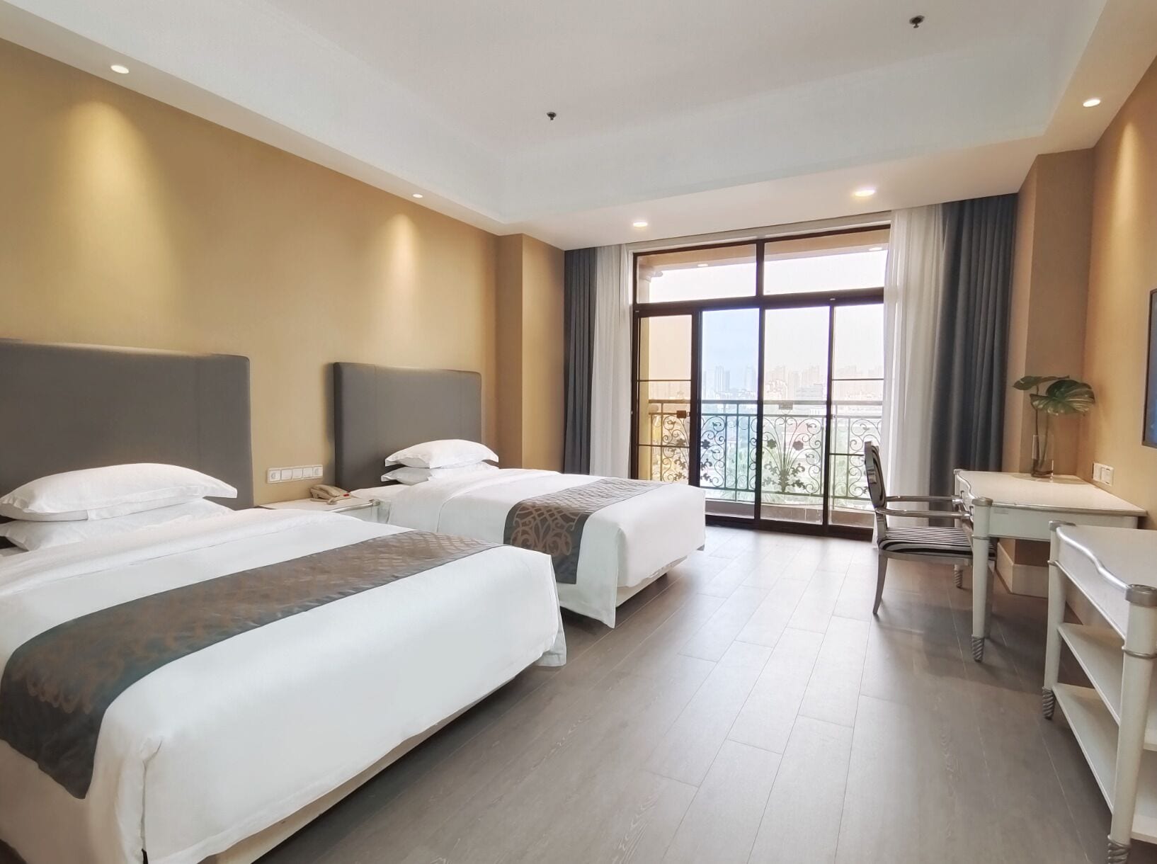 Habitació d'hotel amb dos llits, escriptori i balcó amb vista a la ciutat.