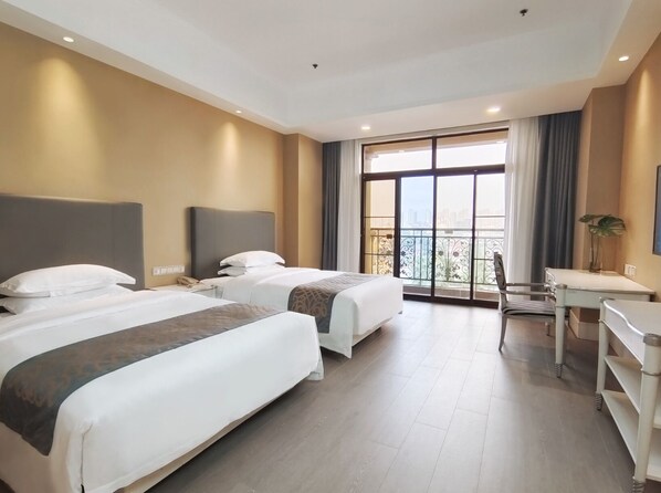 A hotel room with two beds, a desk, and a balcony with a city view.