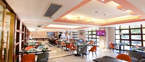 Un restaurante moderno con varias zonas de comedor, ventanas amplias y una pantalla de televisión.