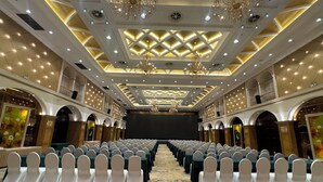 Un salón de banquetes con filas de mesas y sillas, candelabros y una pantalla grande.