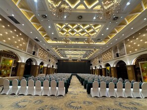 Un salón de banquetes con filas de mesas y sillas, candelabros y una pantalla grande.