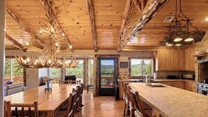 Un vaste espace dédié à la salle à manger, avec une longue table et des chaises en bois, une cuisine dotée de meubles en bois et une vue sur l’extérieur.