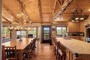 Un vaste espace dédié à la salle à manger, avec une longue table et des chaises en bois, une cuisine dotée de meubles en bois et une vue sur l’extérieur.