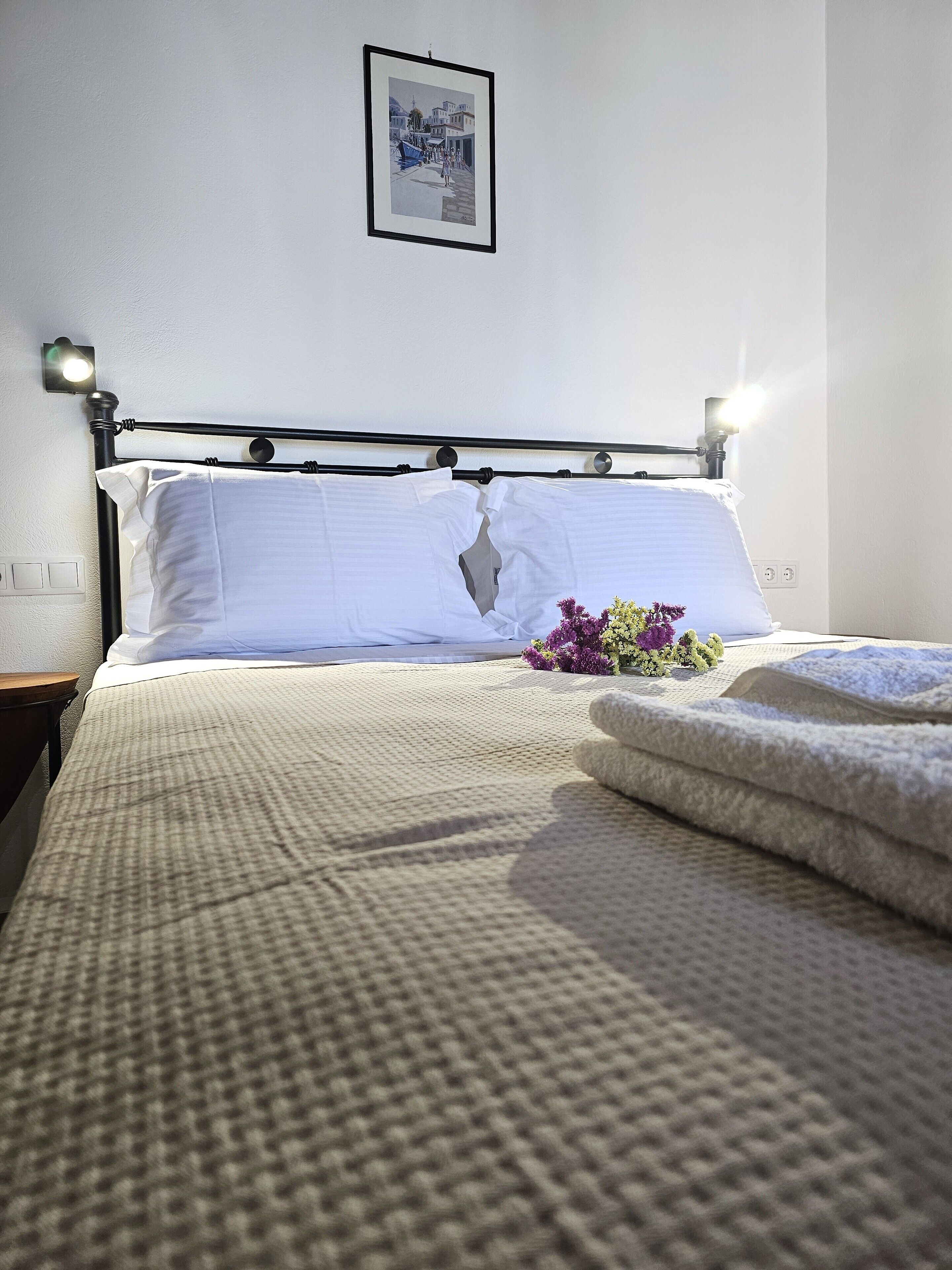 A neatly made bed with a white comforter, pillows, and a floral arrangement.