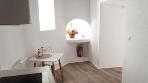 Une petite pièce lumineuse, avec une table blanche, des chaises et une fenêtre ornée d’un panier de fleurs.