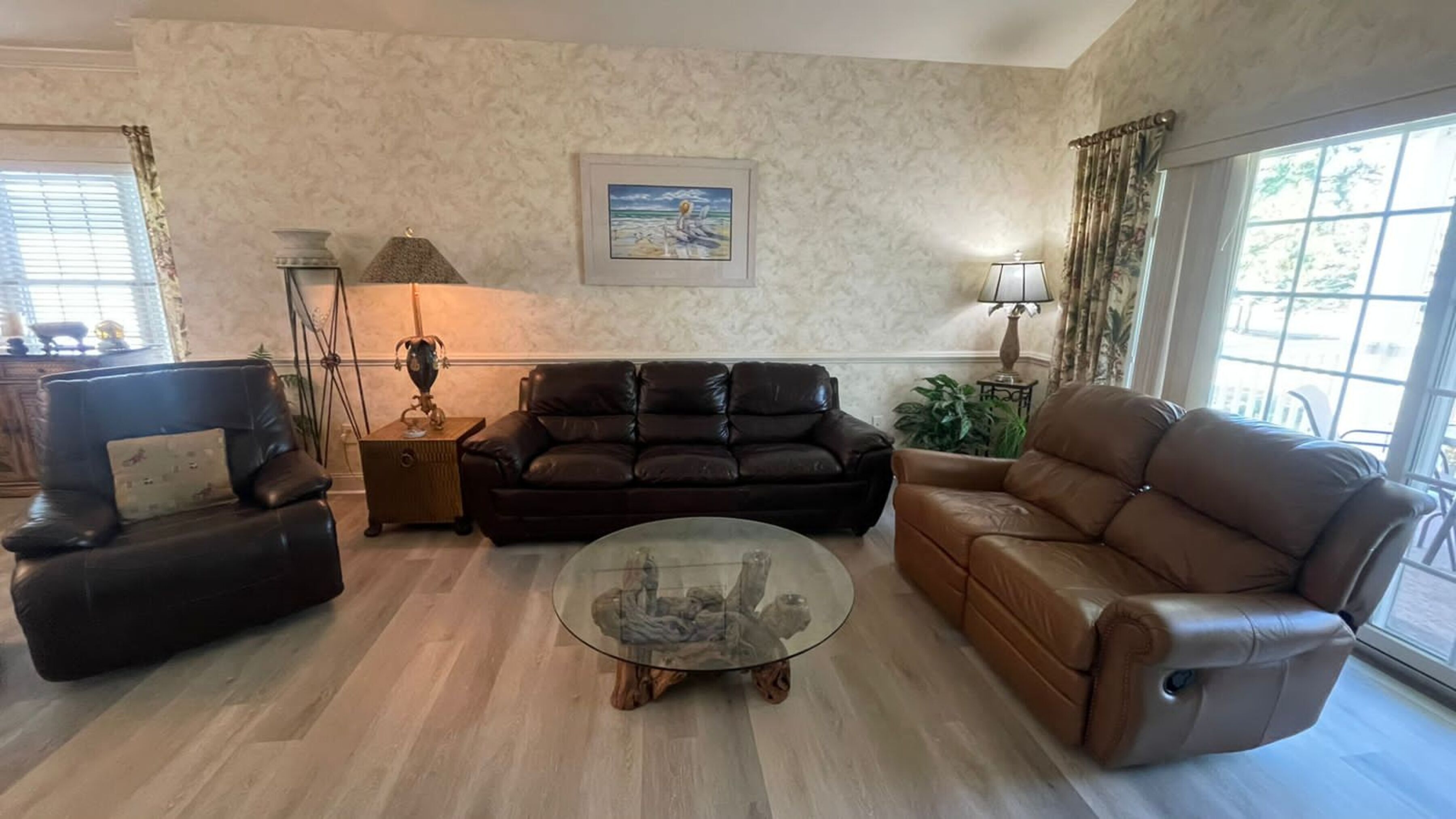 A living room with a brown leather sofa, a glass coffee table, and a wooden side table.