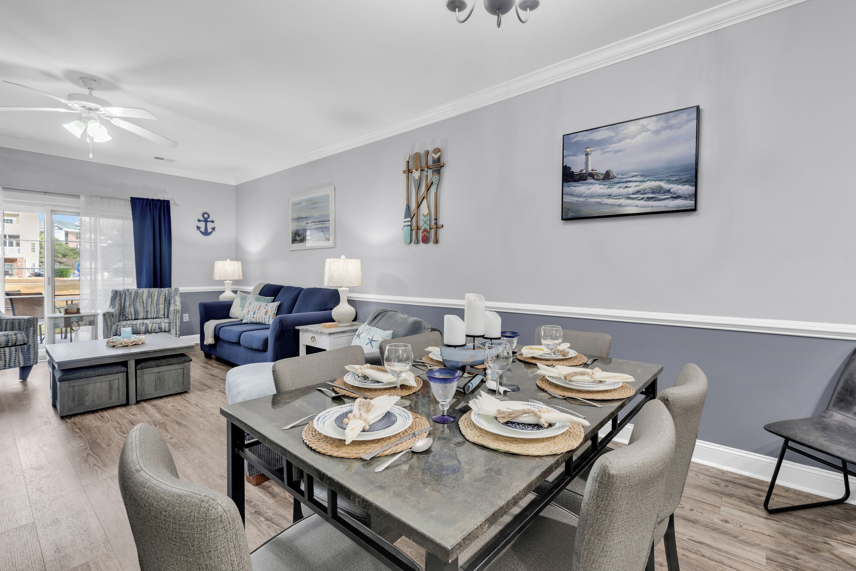 A modern living room with a dining area set for six, featuring a grey and white color scheme, nautical decor, and a view of the city.