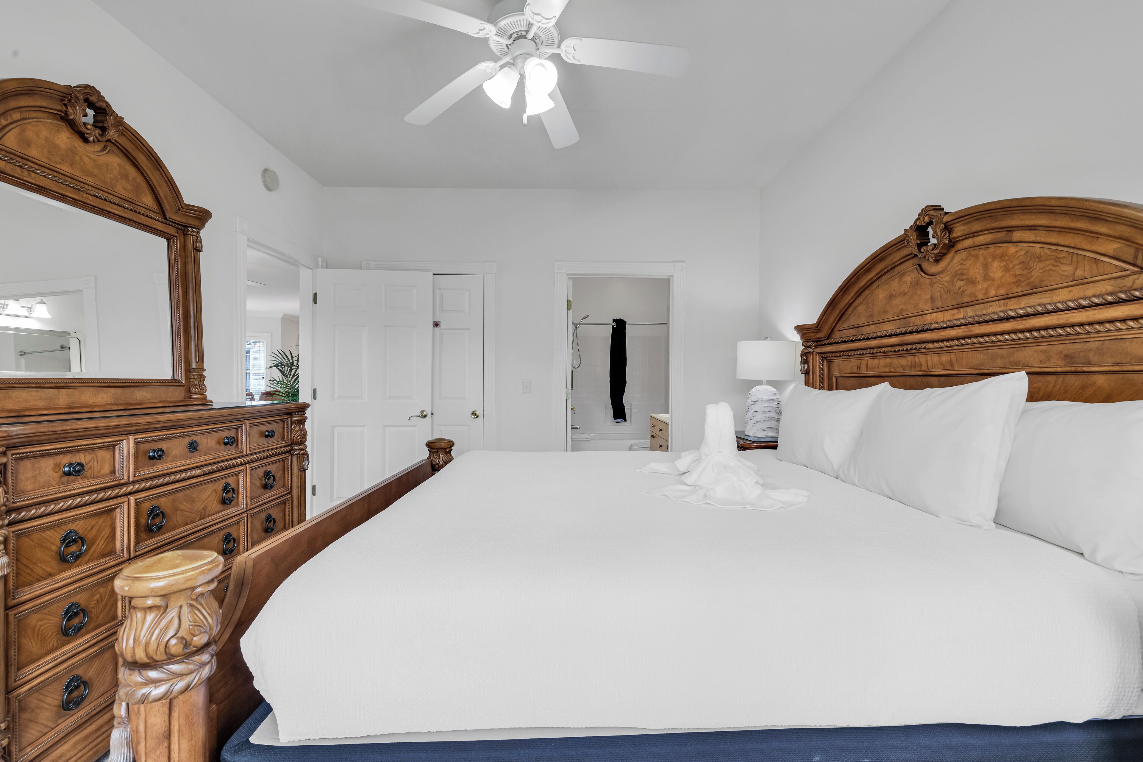 A large bed with a wooden headboard, a ceiling fan, and a dresser with drawers.