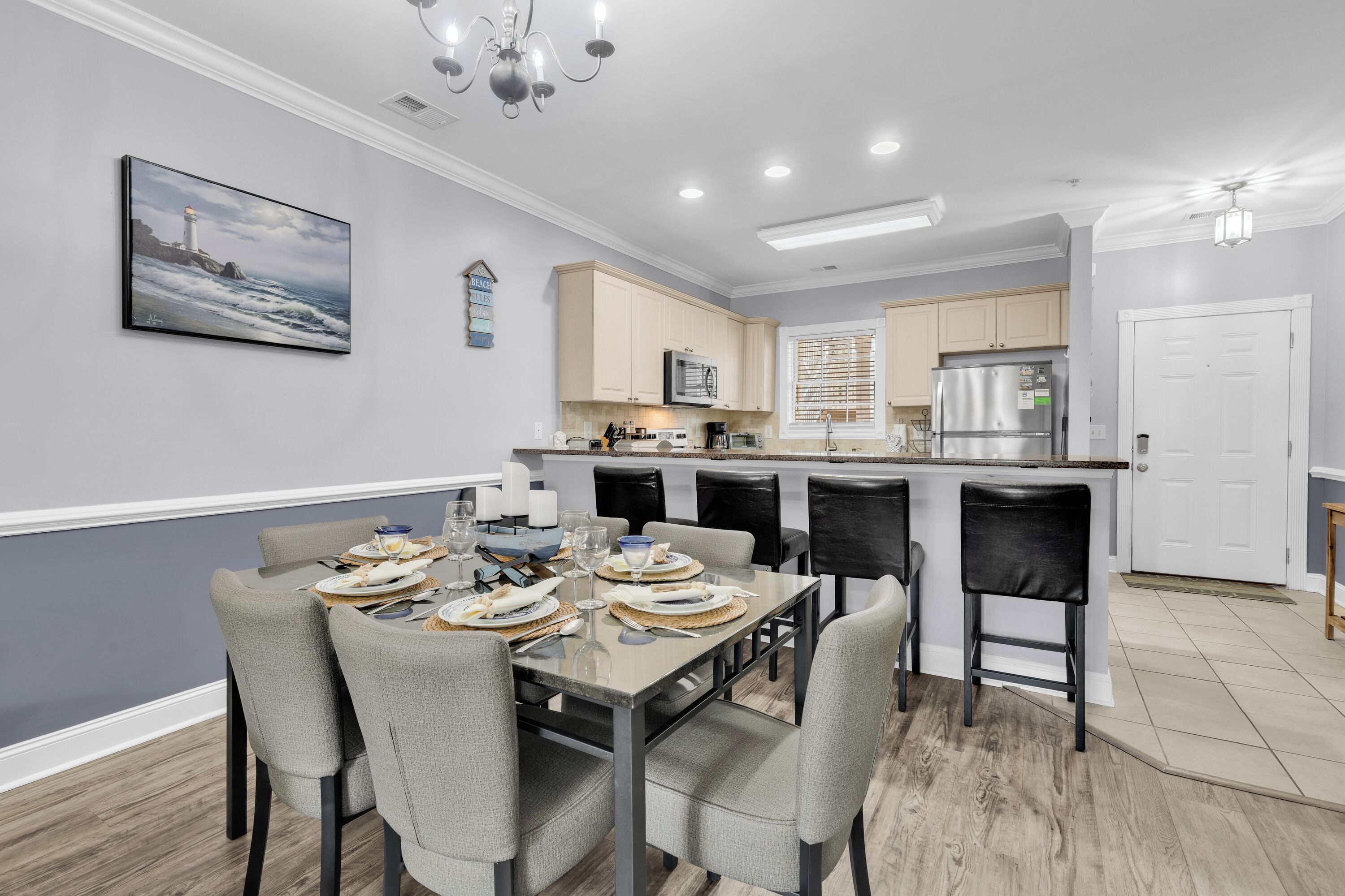 A modern kitchen with a central island, a dining area with a table set for four, and a large painting on the wall.
