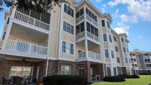 A multi-story apartment building with balconies, brick facade, and a well-maintained lawn. - Magnolia Pointe (Myrtle Beach)