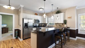 A modern kitchen with white cabinets, stainless steel appliances, and a central island with bar stools. - Magnolia Pointe (Myrtle Beach)
