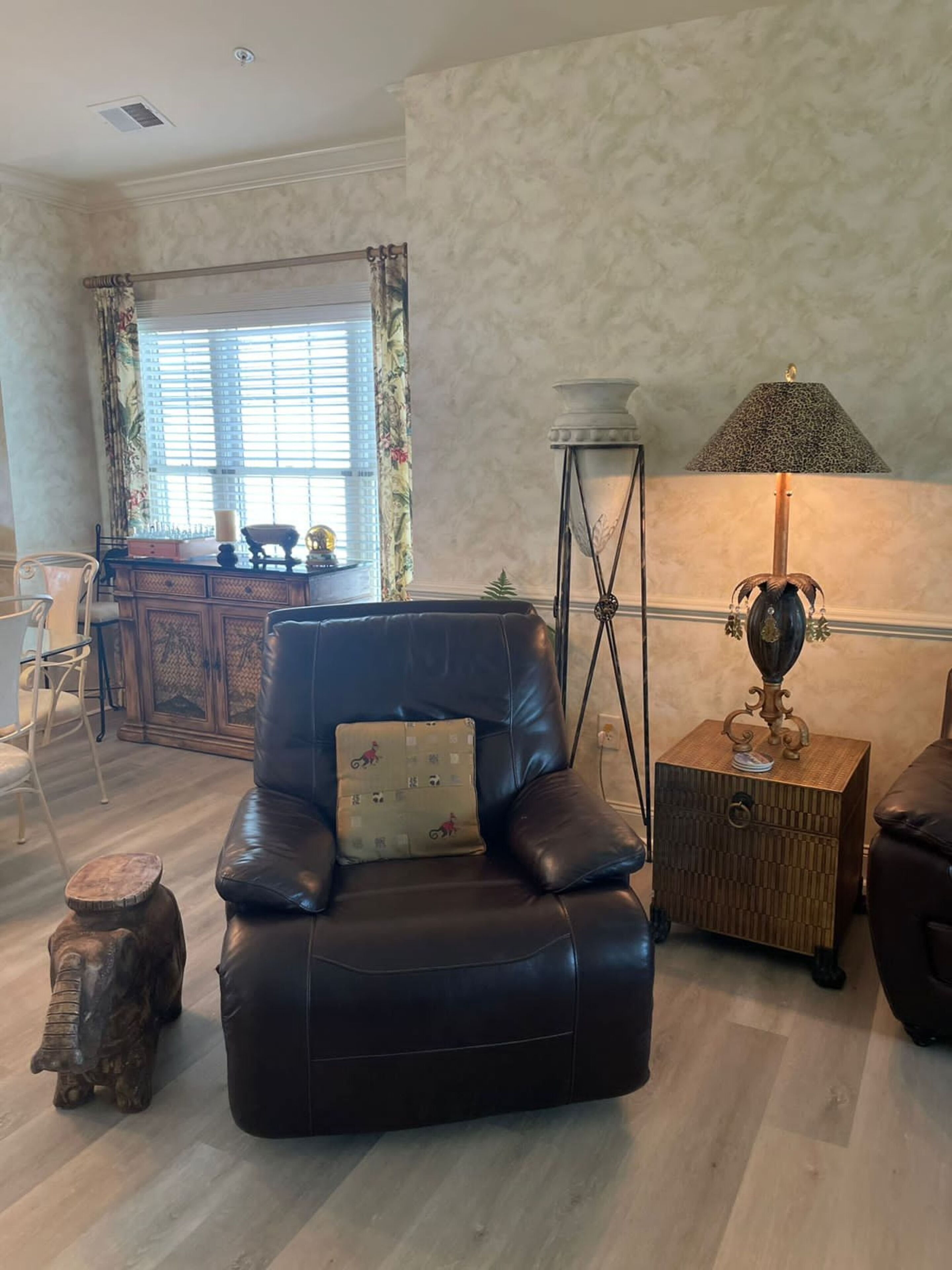A living room with a leather armchair, a small wooden side table with a lamp, and a decorative stool.